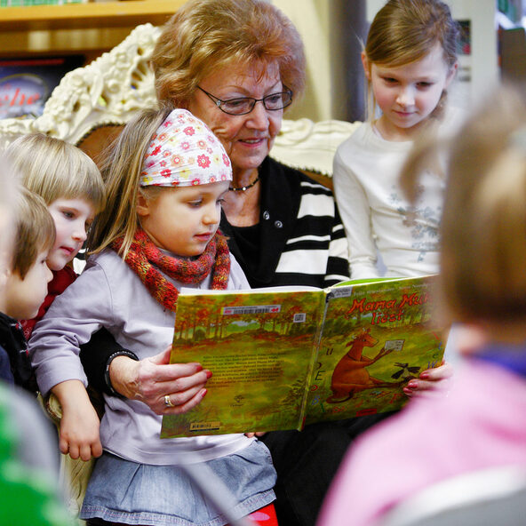 Frau liest Kindern aus einem Buch vor.
