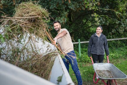 Zwei Teilnehmende am Social Day befüllen einen Container mit Grünschnitt und Unkraut