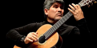 Ein Foto vom Musiker Piraí Vaca: schwarzer Hintergrund, davor der Künstler mit einem schwarzen Langarmshirt bekleidet, während er auf einer Akustikgitarre spielt